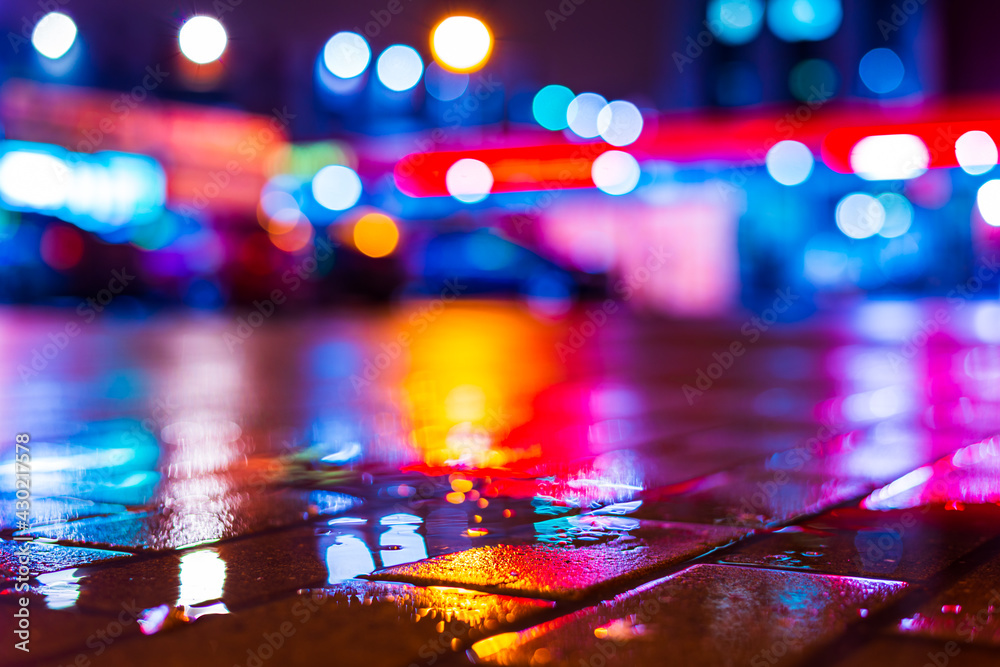 Rainy night in the city. Parking mall with cars. Reflections of shop windows on the wet pavement. Colorful colors. Close up view from the level of the puddle on the pavement