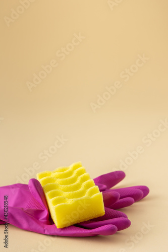 Yellow dishwashing sponge and pink rubber gloves on neutral beige background  cleaning concept