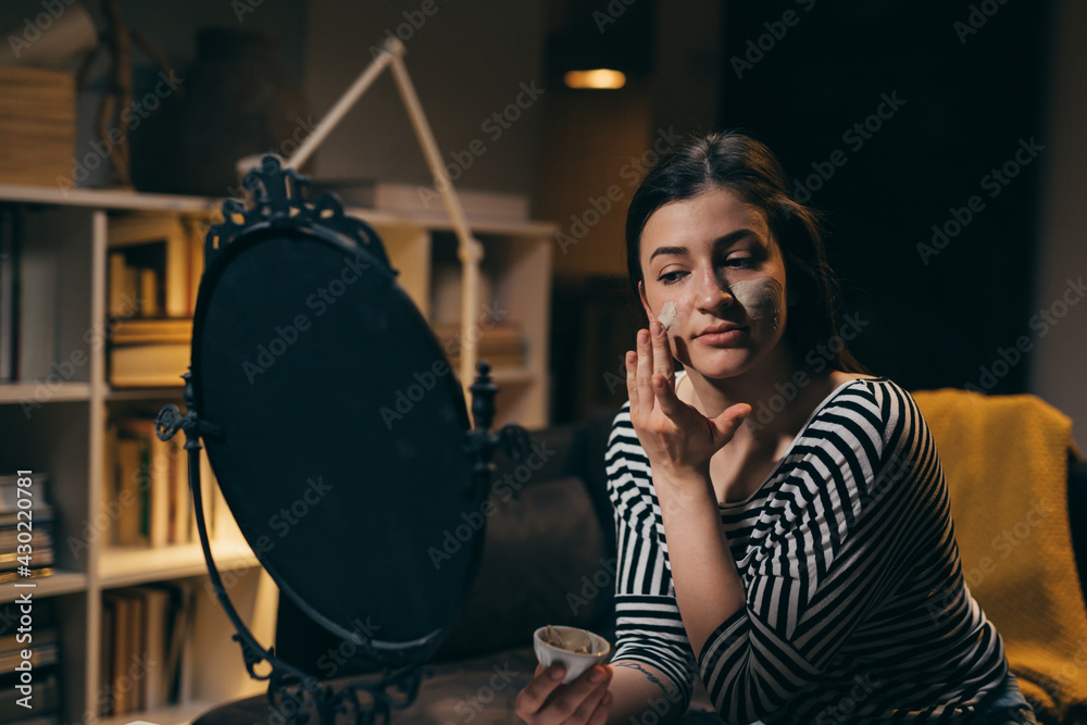 Fototapeta premium woman applying cosmetic face mask at home. evening scene