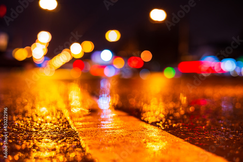 Rainy night in the city. Headlights driving cars. Reflections of street lamps on the wet asphalt. Colorful colors. Close up view from the level of the dividing line.