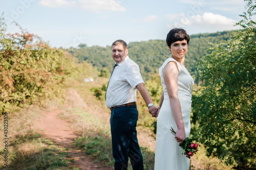 Newlyweds hold hands on the background of the forest