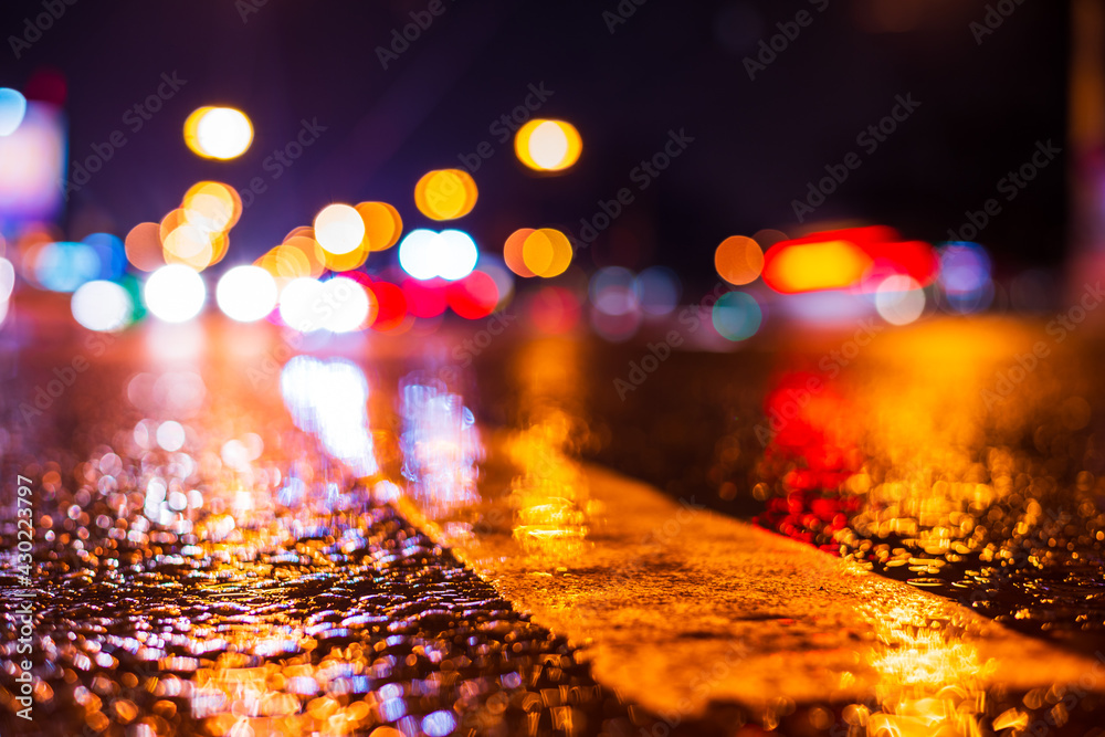 Rainy night in the city. Headlights driving cars. Reflections of street lamps on the wet asphalt. Colorful colors. Close up view from the level of the dividing line. Rainy night in the city. Headlights driving cars. Reflections of street lamps on the wet asphalt. Colorful colors. Close up view from the level of the dividing line.