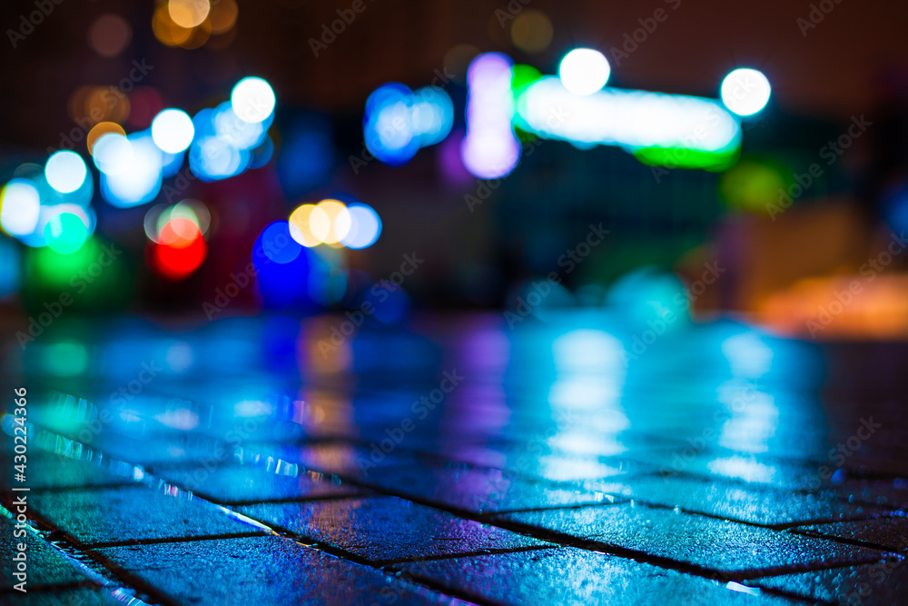 Rainy night in the city. Deserted parking mall. Reflections of shop windows on the wet pavement. Colorful colors. Close up view from the pavement level.