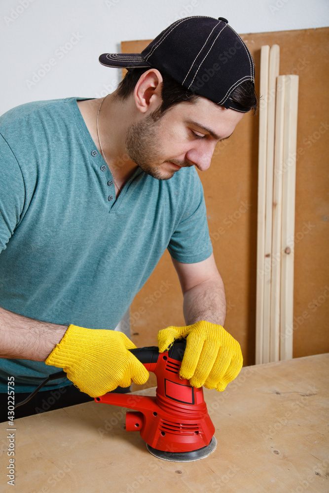 Renovation or DIY work. Beginner skills. Man grinds a board or plywood with a grinder. Person learns to work with a grinder. Carpenter working in workshop. Handmade concept. New normal. wooden crafts Renovation or DIY work. Beginner skills. Man grinds a board or plywood with a grinder. Person learns to work with a grinder. Carpenter working in workshop. Handmade concept. New normal. wooden crafts