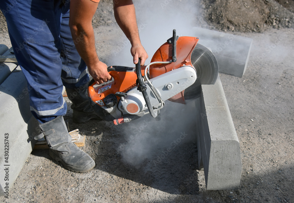 A worker saws a concrete curb with a circular saw.