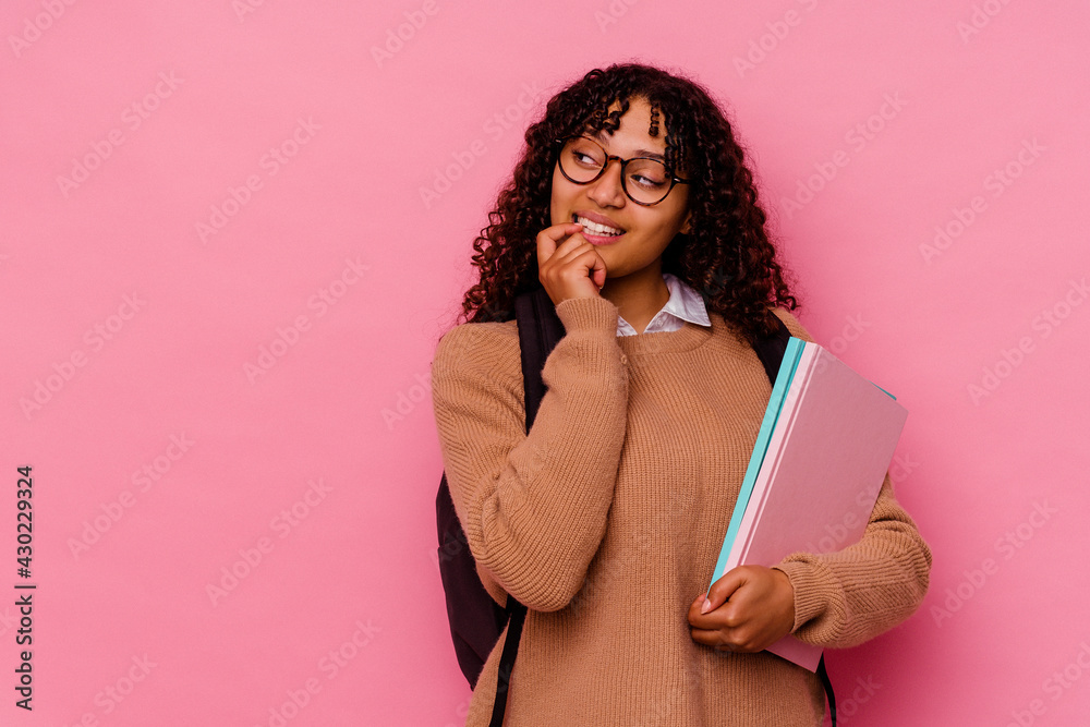Young student mixed race woman isolated on pink background relaxed thinking about something looking at a copy space. Young student mixed race woman isolated on pink background relaxed thinking about something looking at a copy space.