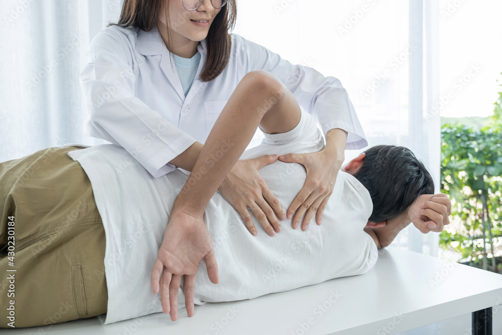 Female doctor hands doing physical therapy By extending the back of a male patient Female doctor hands doing physical therapy By extending the back of a male patient