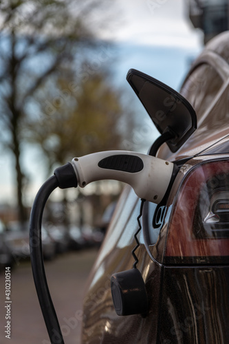 Modern electric car being charged in the dutch street, Close up of the plugged charging plug © Milos