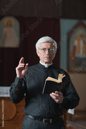 Canvas Print Portrait of senior priest reading the Bible during a mass in the church
