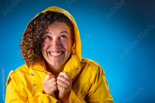 Mujer joven cabello enrulado sonríe con impermeable amarillo sobre fondo azul