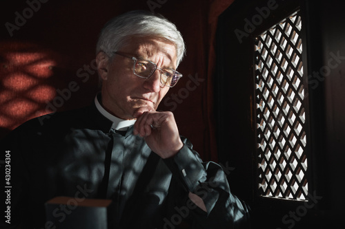 Senior priest sitting behind the grid and listening the confession in the church