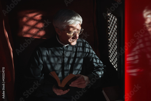 Senior priest sitting with the Bible in confessional and listening to confession photo