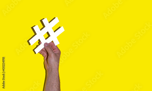 Man's hand holding a white hash on a yellow background - social media day concept