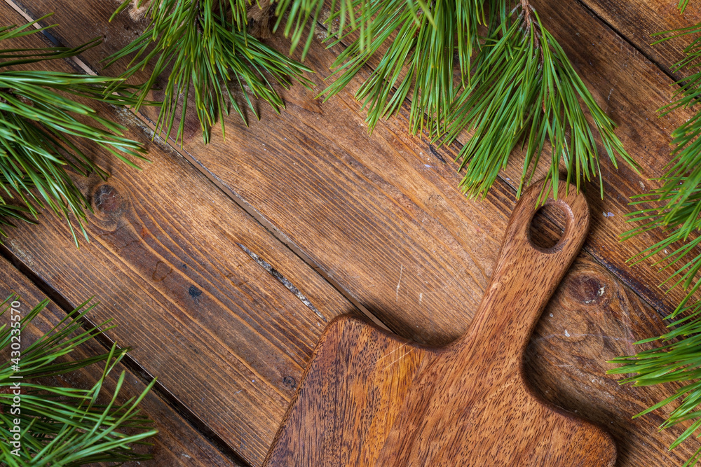 Fragment cutting board on a wooden table background surrounded by pine branches, top view. Fragment cutting board on a wooden table background surrounded by pine branches, top view.