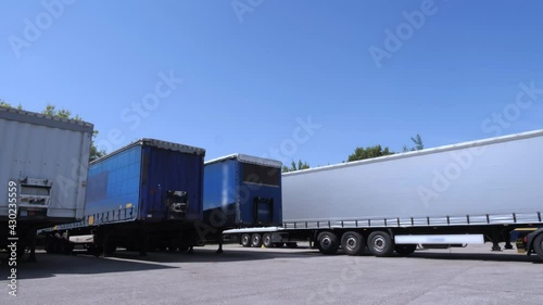 White lorry with cargo trailer drives back into parking place and parks with other cargo trailers.