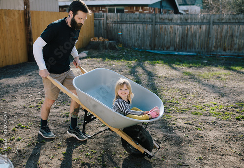 Father pushing daughter in a wheelbarrow around the back yard
