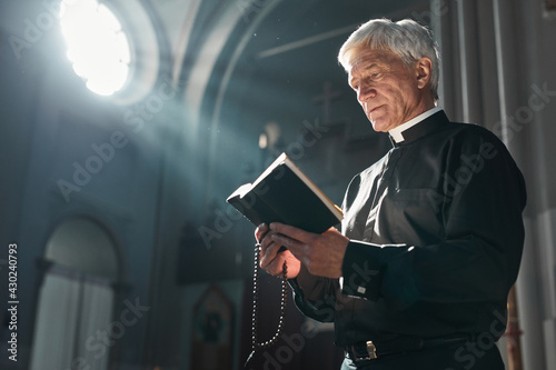 Fototapeta Senior priest reading the Bible during ceremony while standing in the church