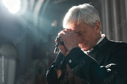 Senior priest holding rosary beads praying while sitting in the church