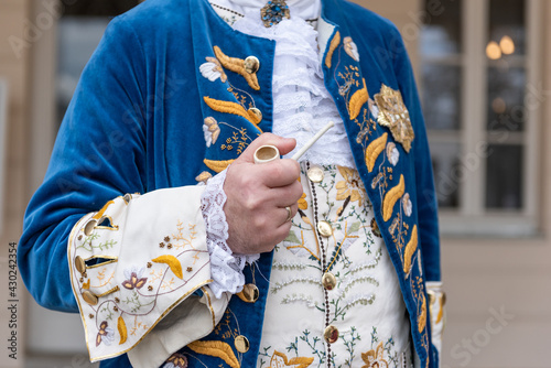 The details of man dressed in a baroque costume. A hand holding a pipe, golden buttons, vest and decorative hems.