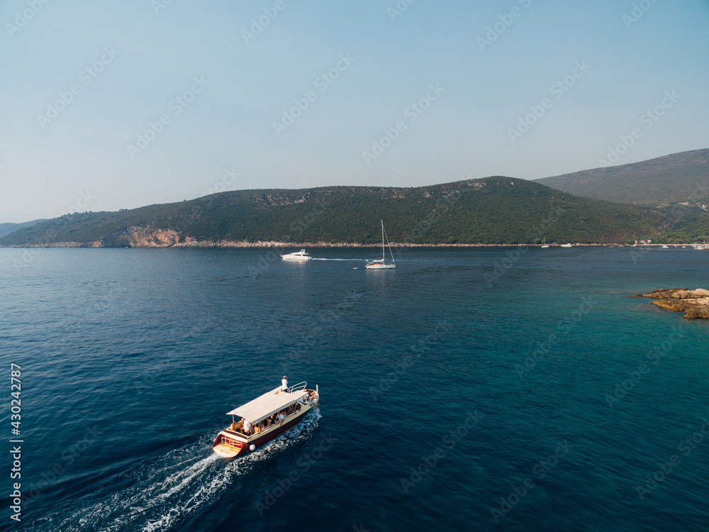 Pleasure white yacht with a canopy and people on board sails along the sea to the shore