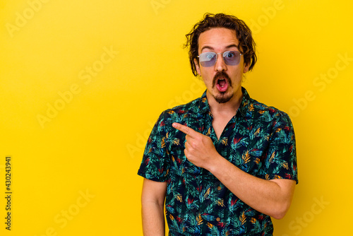 Young caucasian man wearing summer clothes isolated on yellow background pointing to the side