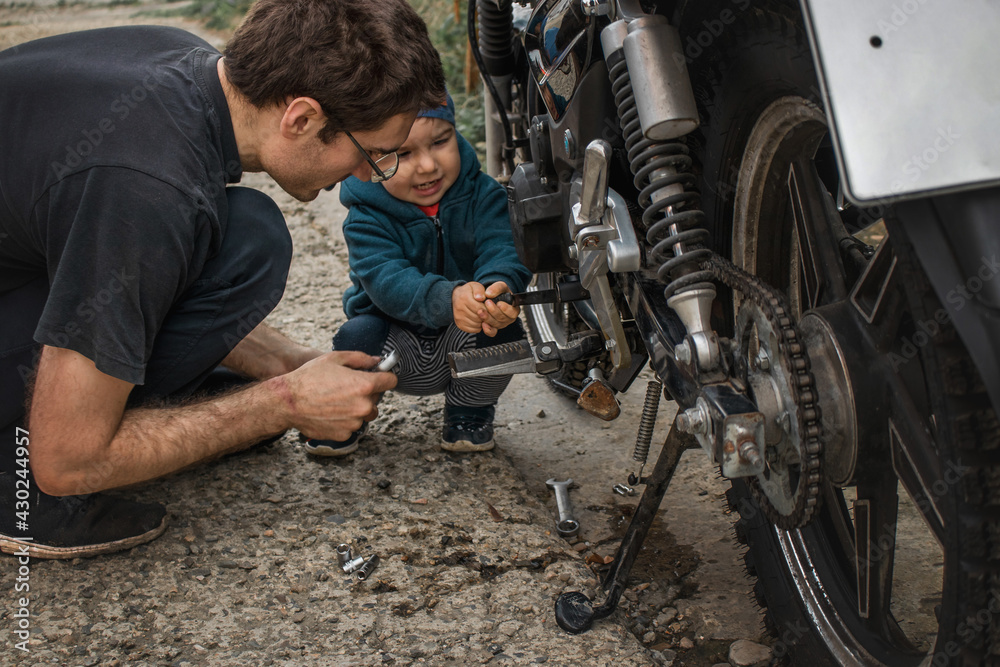 A father on the street shows his young son how to fix a motorcycle. Father-son communication.