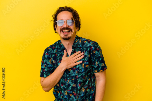 Young caucasian man wearing summer clothes isolated on yellow background laughs out loudly keeping hand on chest.