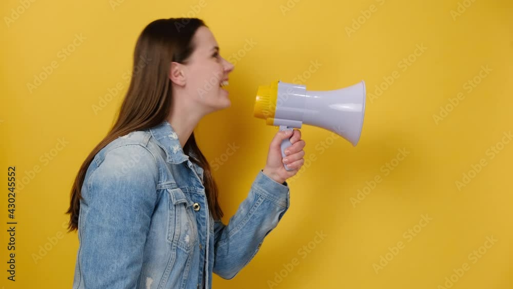 Side view of cheerful caucasian young woman screaming in megaphone turn around camera showing thumb up like, wears denim jacket, isolated over yellow studio background wall. People lifestyle concept Side view of cheerful caucasian young woman screaming in megaphone turn around camera showing thumb up like, wears denim jacket, isolated over yellow studio background wall. People lifestyle concept