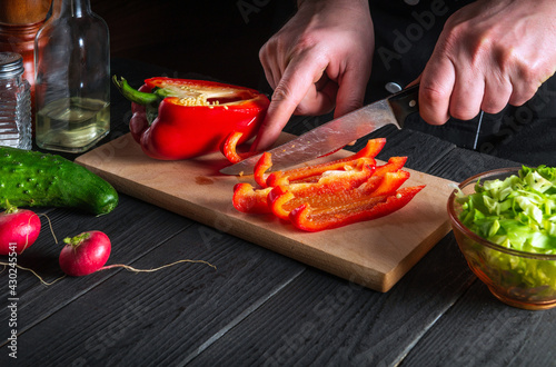 Close-up of chef or cook hands cutting peppers on cutting board. Professional preparation of salad in the kitchen in a restaurant or cafe
