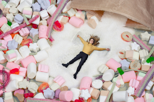 the girl lies in a heap of sugar and sweets. the woman spread her arms out to the sides and enjoys candies. excessive sugar intake