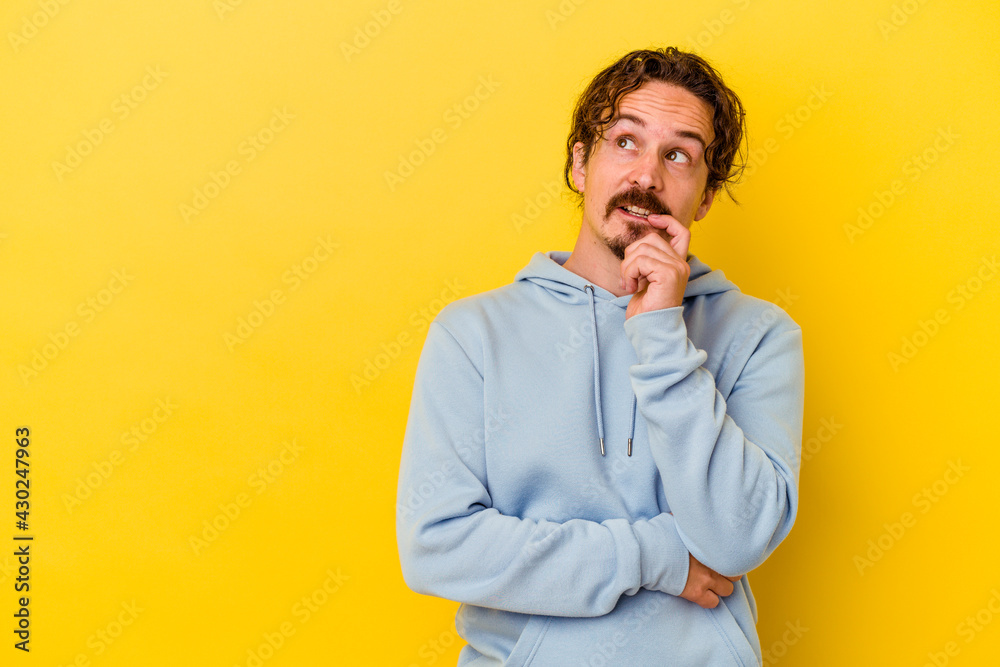 Young caucasian man isolated on yellow background relaxed thinking about something looking at a copy space. Young caucasian man isolated on yellow background relaxed thinking about something looking at a copy space.