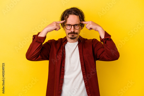 Young caucasian man isolated on yellow background focused on a task, keeping forefingers pointing head.