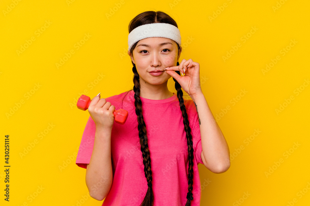Young sport chinese woman isolated on yellow background with fingers on lips keeping a secret. Young sport chinese woman isolated on yellow background with fingers on lips keeping a secret.