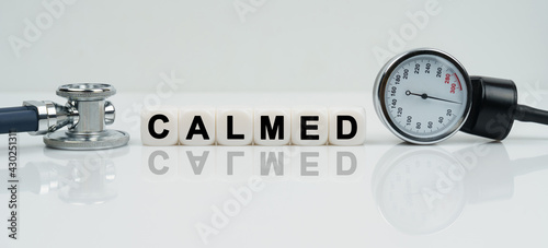 On a reflective white surface lies a stethoscope and cubes with the inscription - CALMED