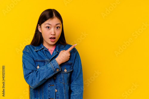 Young chinese woman isolated on yellow background pointing to the side © Asier