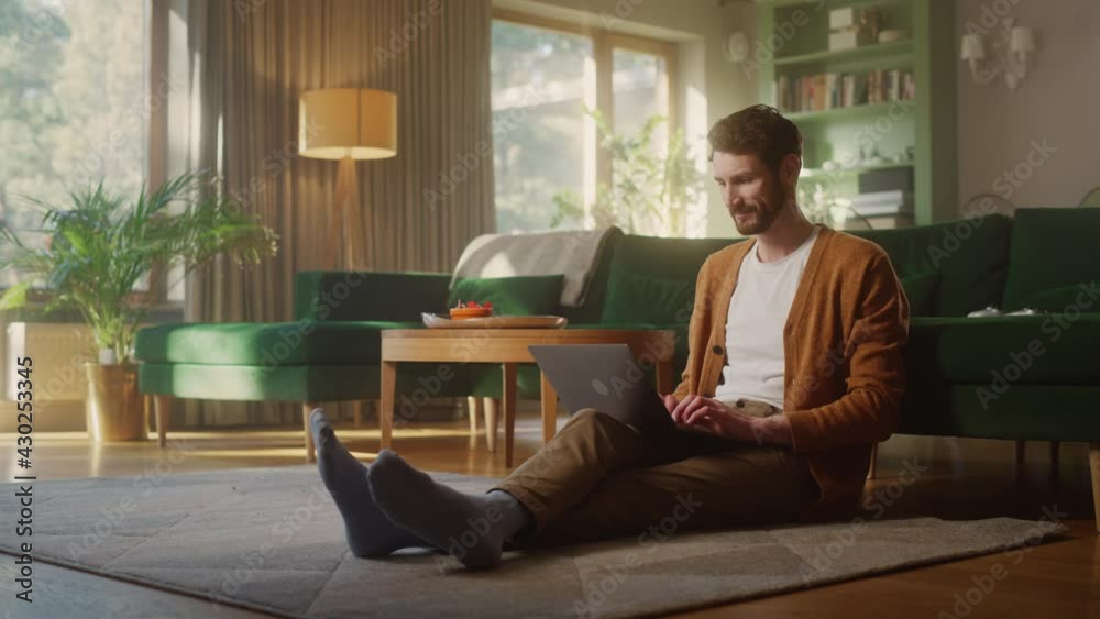 Handsome Happy Man Using Laptop Does Remote Work from Living Room. Male Sitting on Floor Uses Internet, Writes Project Report. Effective and Productive Distant Worker from Home. Full Shot Handsome Happy Man Using Laptop Does Remote Work from Living Room. Male Sitting on Floor Uses Internet, Writes Project Report. Effective and Productive Distant Worker from Home. Full Shot