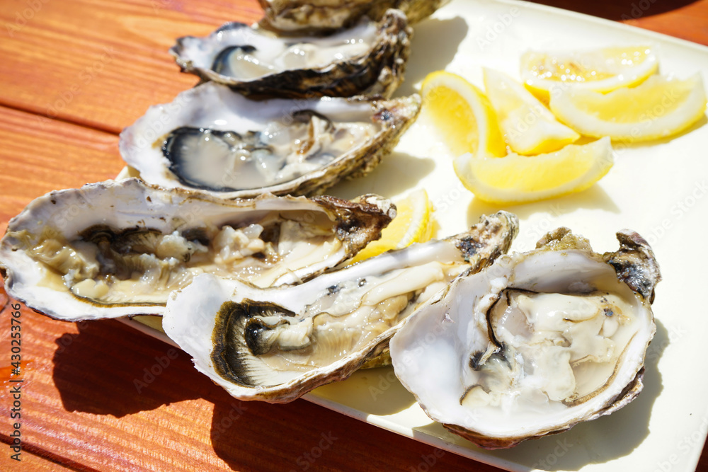 Fresh oysters in a plate with lemons on a wooden table, close-up