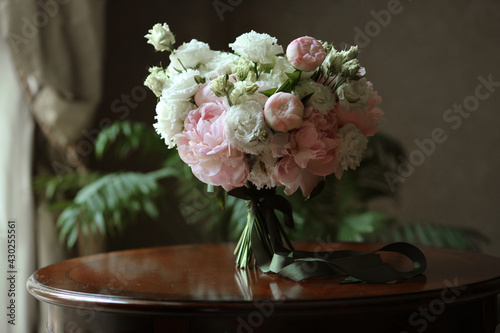 Bridal bouquet of white roses and peonies flowers with green festive ribbon in the morning before the wedding ceremony photo