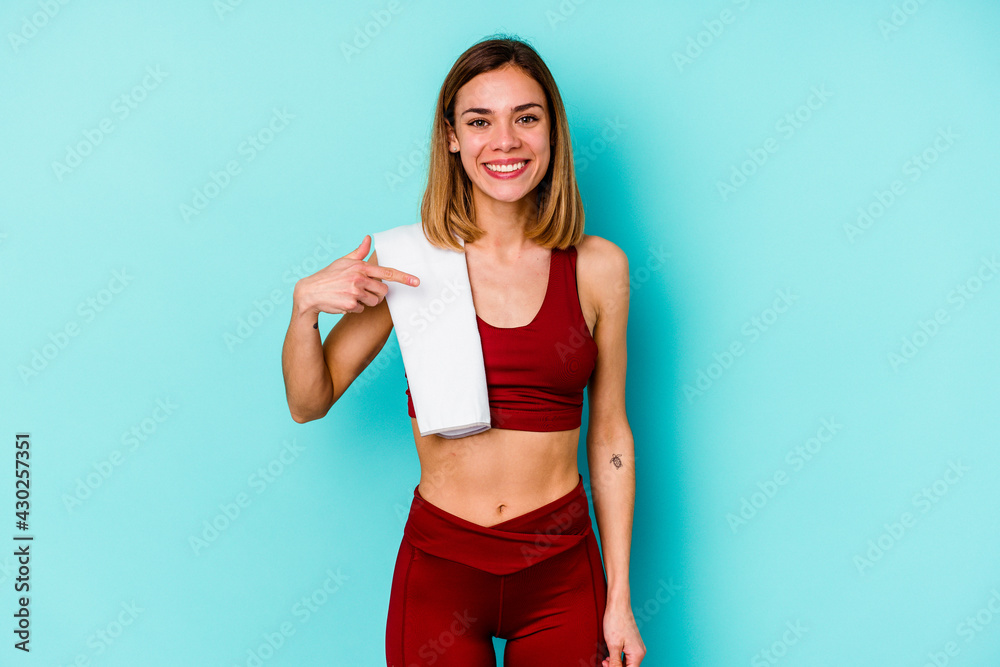 Young sport caucasian woman isolated on blue background person pointing by hand to a shirt copy space, proud and confident