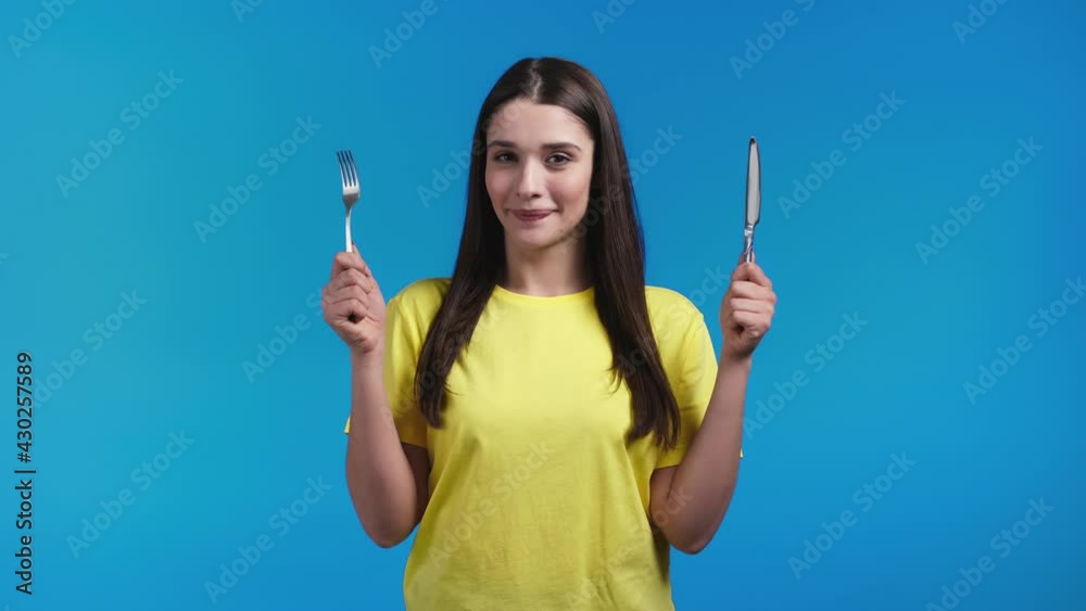 Portrait of hungry woman with fork and knife. Lady waiting for serving dinner dishes with cutlery on blue studio background. Portrait of hungry woman with fork and knife. Lady waiting for serving dinner dishes with cutlery on blue studio background.
