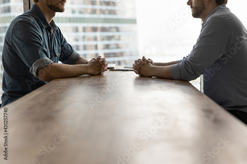Determined young businessmen sit opposite at desk face each other talk speak at business meeting or negotiations. Male rivals or opponents have briefing in office. Rivalry, confrontation concept. photo