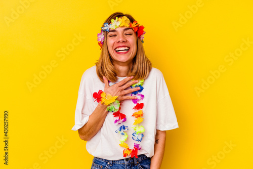 Young caucasian woman celebrating a hawaiian party isolated on yellow background laughs out loudly keeping hand on chest.