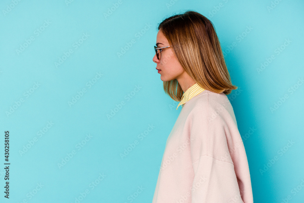 Young student caucasian woman isolated on blue background gazing left, sideways pose. Young student caucasian woman isolated on blue background gazing left, sideways pose.