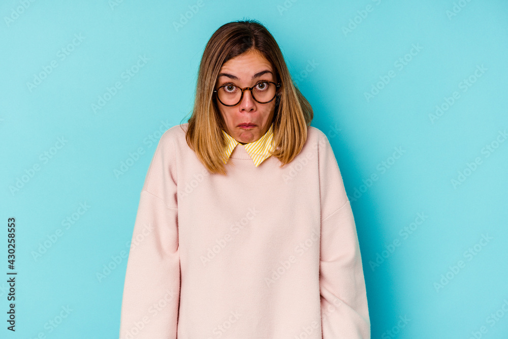 Young student caucasian woman isolated on blue background shrugs shoulders and open eyes confused. Young student caucasian woman isolated on blue background shrugs shoulders and open eyes confused.