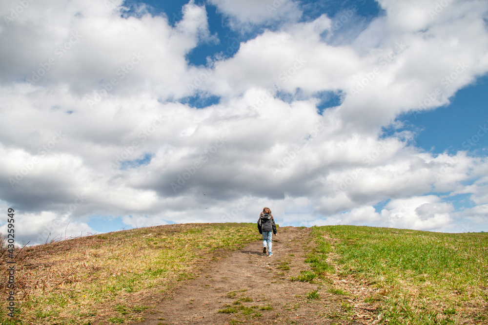 Child walking up a grassy hill toward a cloudy sky