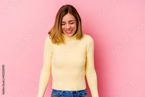 Young caucasian woman isolated on pink background laughs and closes eyes  feels relaxed and happy.