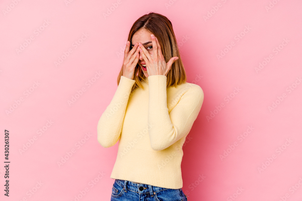 Young caucasian woman isolated on pink background blink through fingers frightened and nervous.