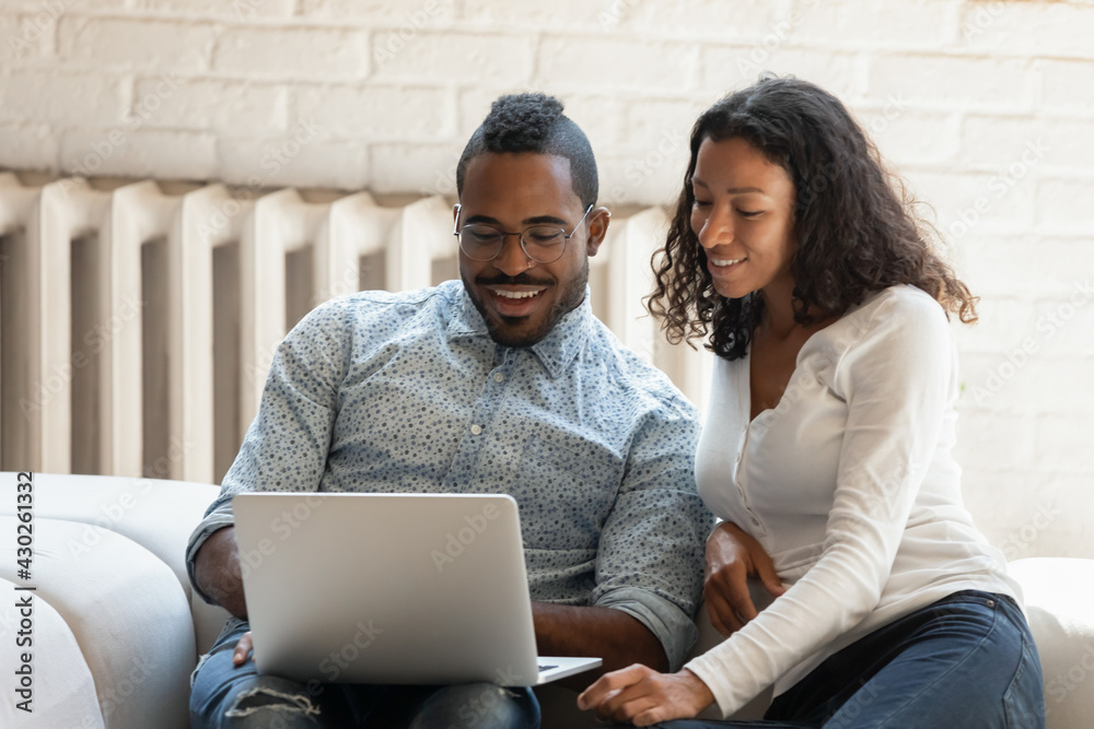 Happy black mixed race couple using laptop at home. Millennial man and woman resting on sofa with computer, shopping online, watching movie together, talking via video call, using bank app for payment Happy black mixed race couple using laptop at home. Millennial man and woman resting on sofa with computer, shopping online, watching movie together, talking via video call, using bank app for payment