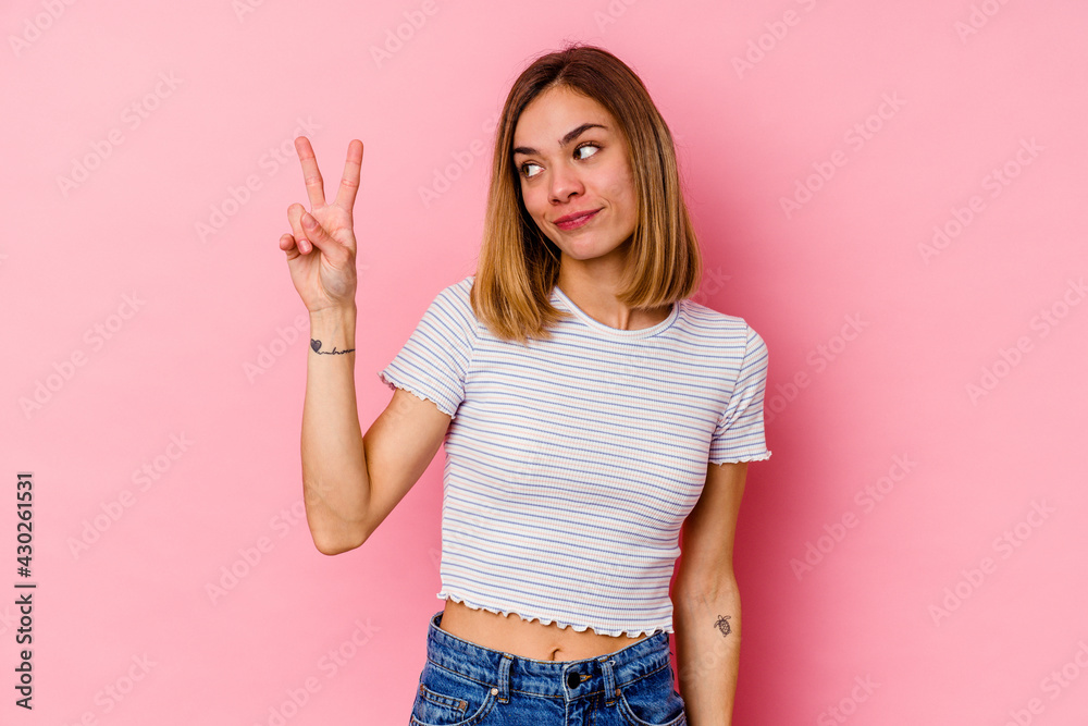 Young caucasian woman isolated on pink background joyful and carefree showing a peace symbol with fingers. Young caucasian woman isolated on pink background joyful and carefree showing a peace symbol with fingers.