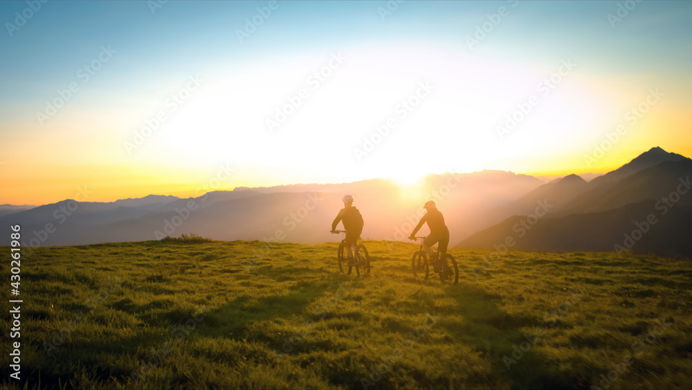 Mother and daughter cycling uphill with mountain bikes at a sunset. Mother and daughter cycling uphill with mountain bikes at a sunset.